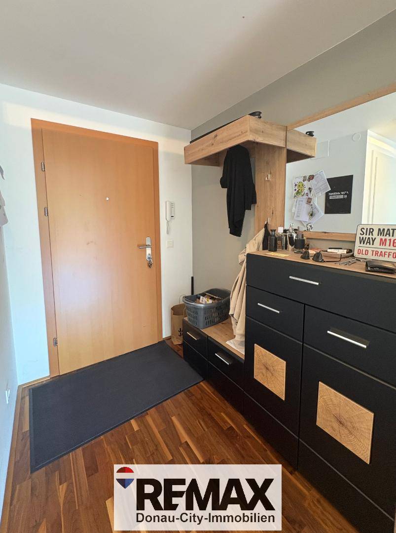Eingangsbereich mit Holzboden, Garderobe und dunklen Möbeln, die Stauraum bieten.