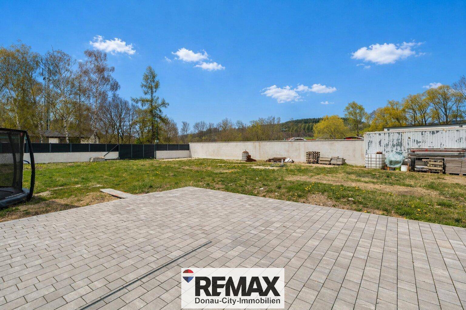 Große gepflasterte Terrasse grenzt an eine weitläufige Rasenfläche im Gartenbereich.