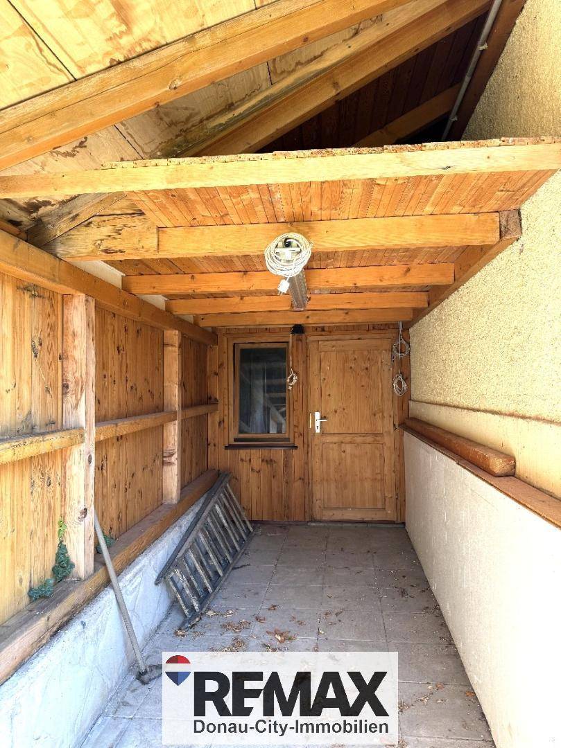 Überdachter Außenbereich oder Schuppen mit Holzwänden und Fliesenboden, ideal für Lagerung.