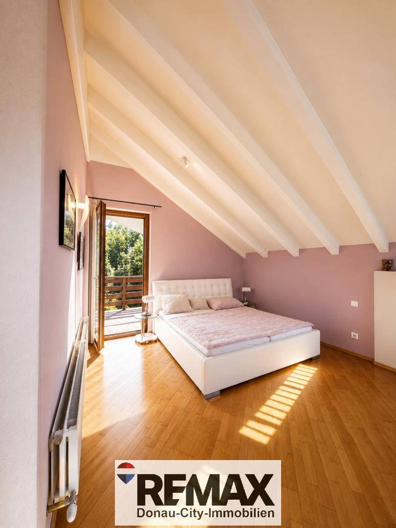 Gemütliches Schlafzimmer mit Doppelbett, rosa Wänden, Holzboden und Zugang zu einem Balkon oder einer Terrasse.