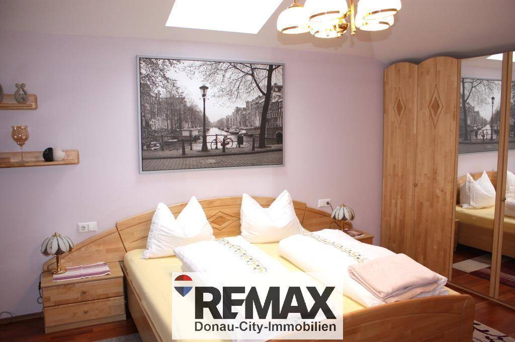 Schlafzimmer mit hellem Holzdoppelbett, Spiegelschrank und einem Dachfenster für natürliches Licht.