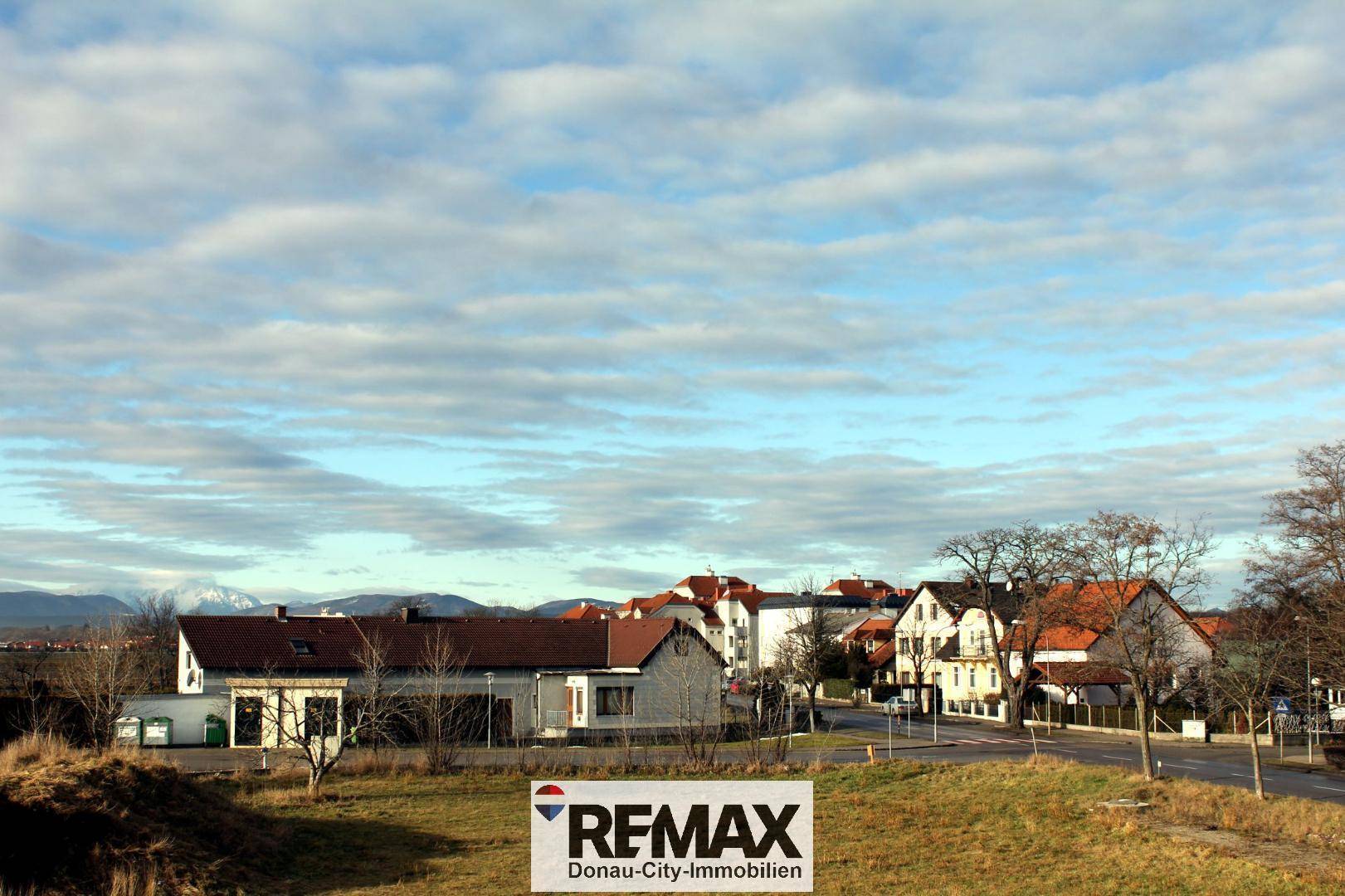 Weitläufige Landschaft mit ländlicher Bebauung und Bergen im Hintergrund unter bewölktem Himmel.
