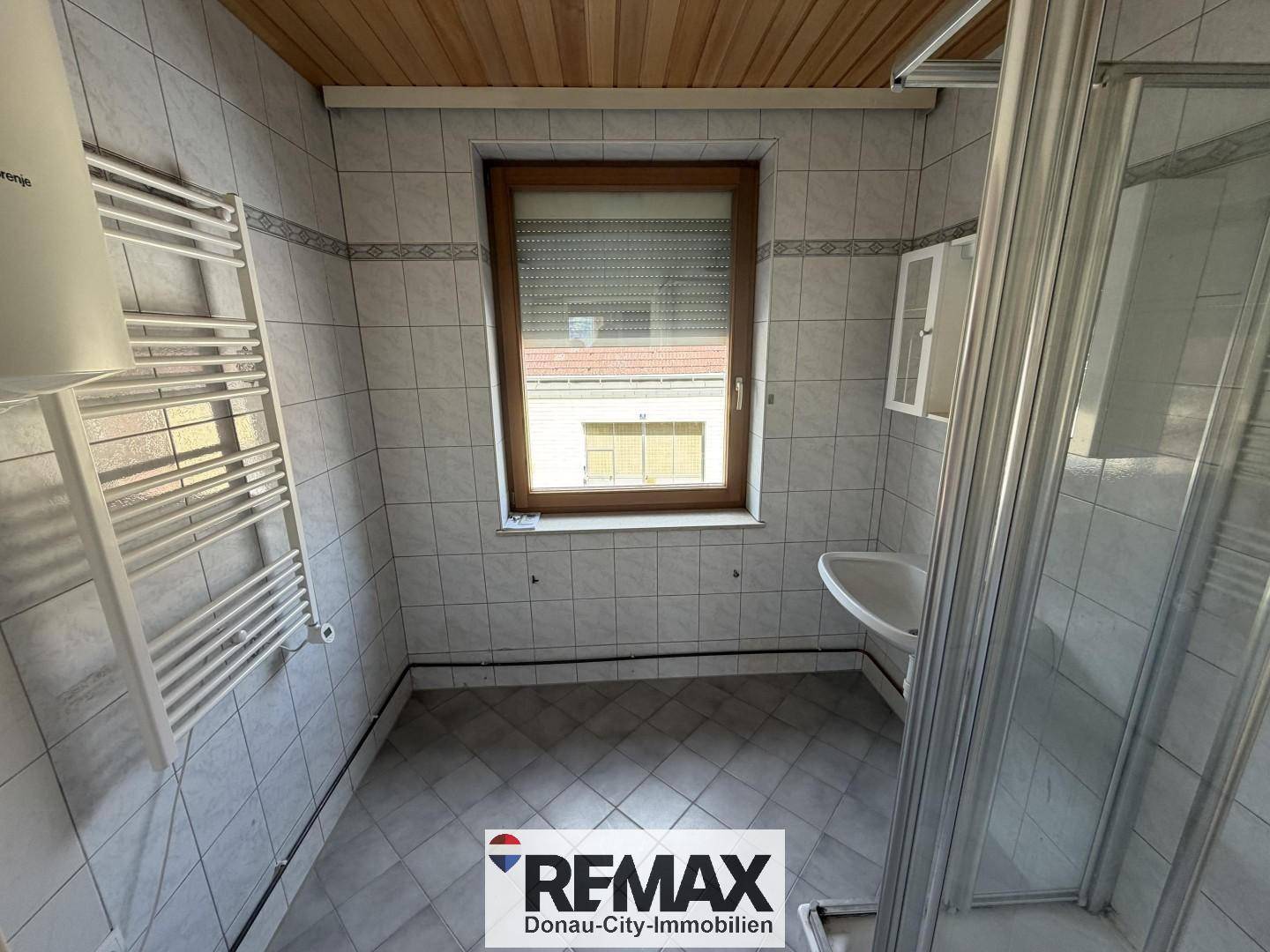 Badezimmer mit Fliesen, Duschkabine, Fenster und beheiztem Handtuchhalter, hell und funktional.