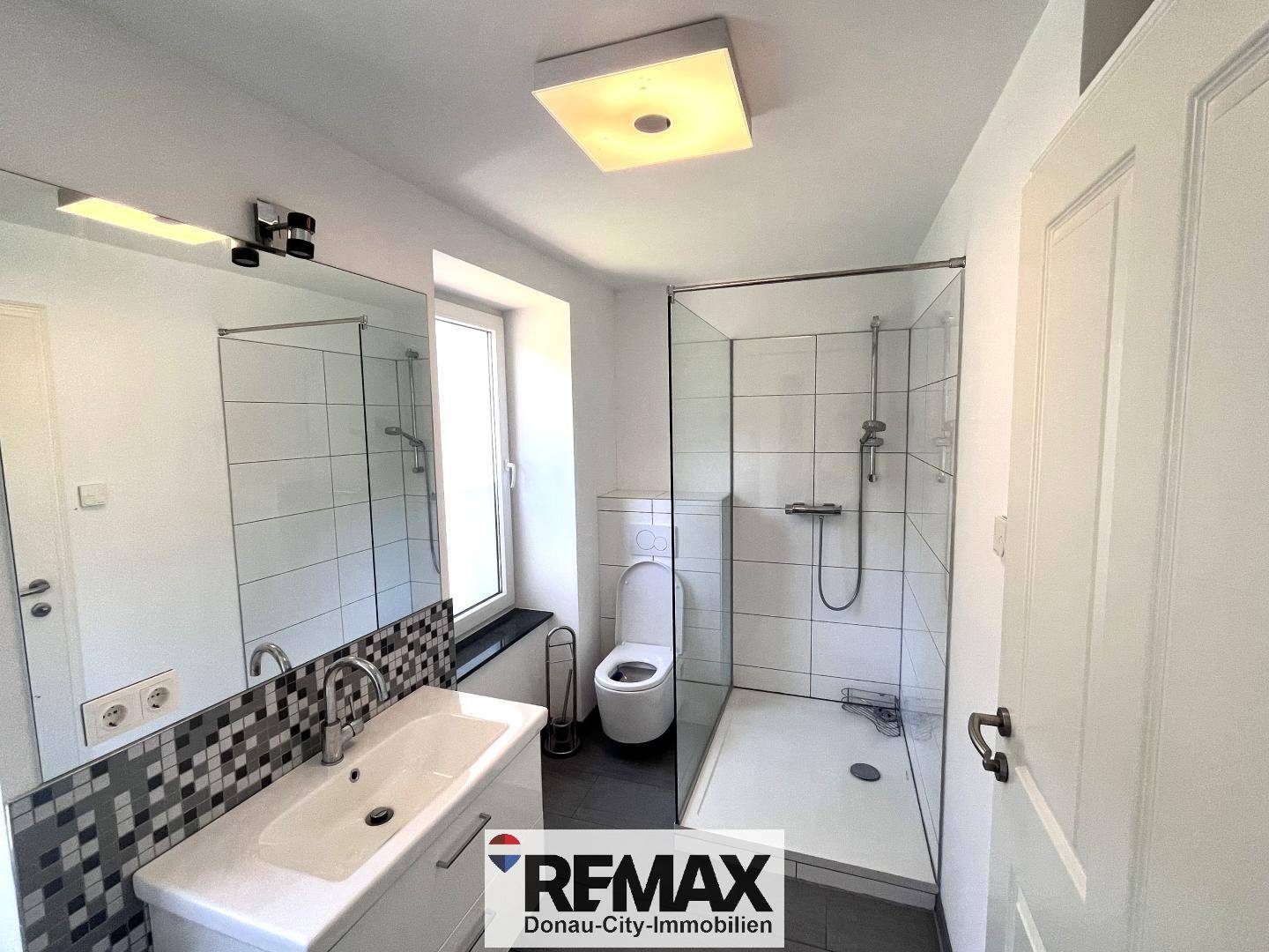 Modernes Badezimmer mit ebenerdiger Dusche, WC und einem großen Spiegel.