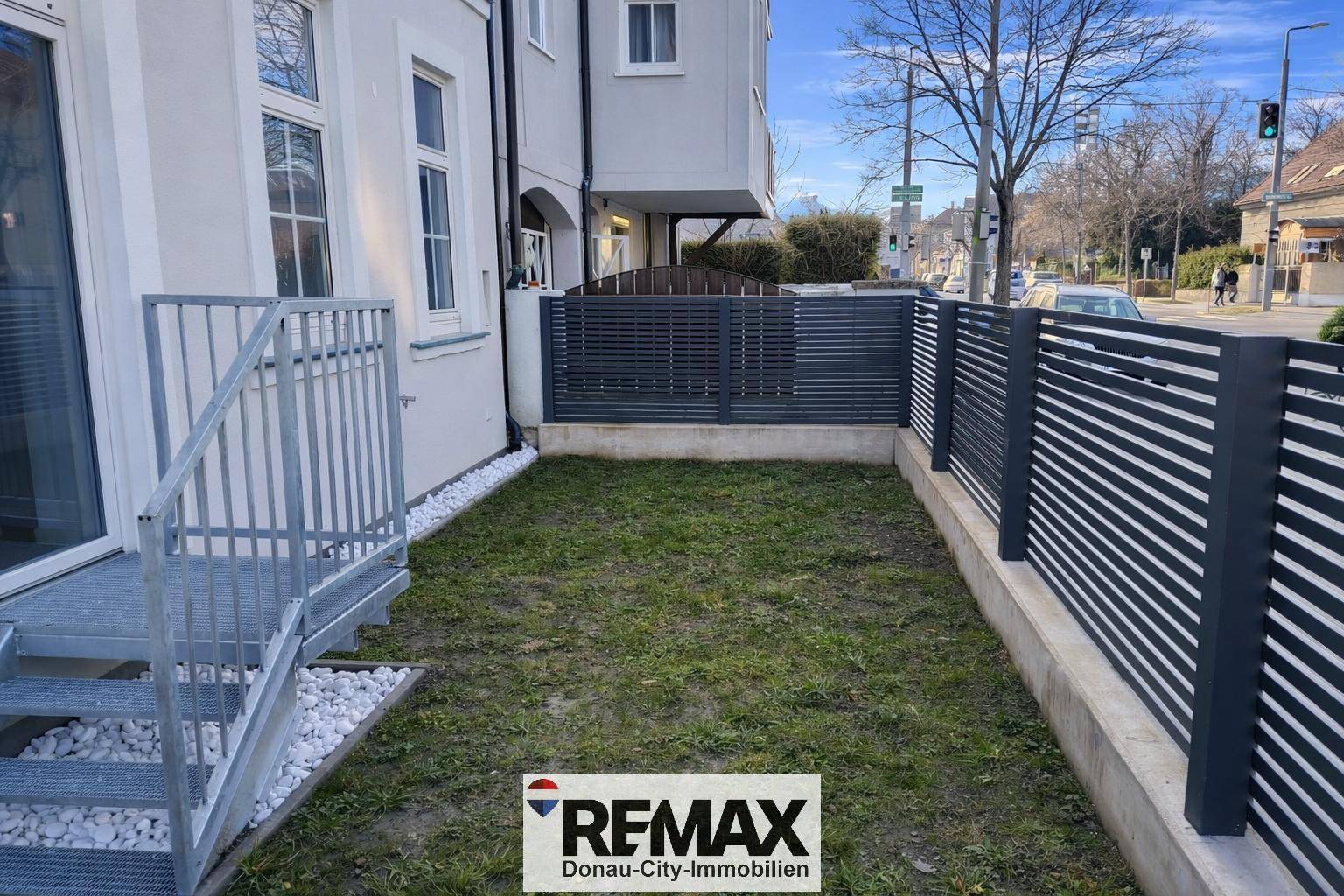 Gepflegter Gartenabschnitt mit Rasen, modernem Zaun und Treppenzugang zur Immobilie.