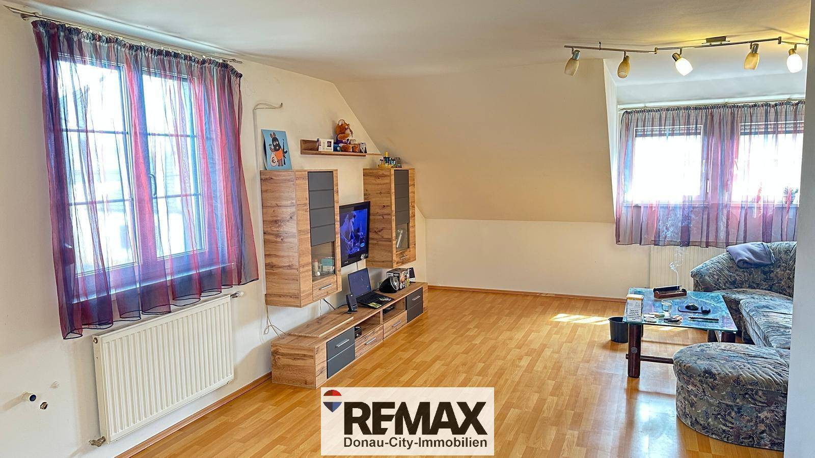 Helles Wohnzimmer im Dachgeschoss mit schrägen Wänden, Laminatboden und moderner Einrichtung.