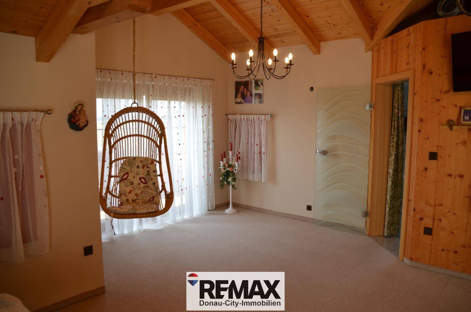Helles Schlafzimmer mit Holzbalken, einem Hängesessel und einer modernen Glastür zu einem angrenzenden Raum.