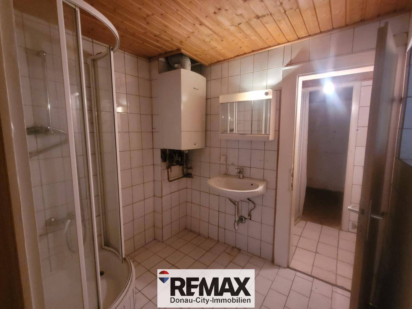 Badezimmer mit Duschkabine, Waschbecken, Boiler und Holzdecke.