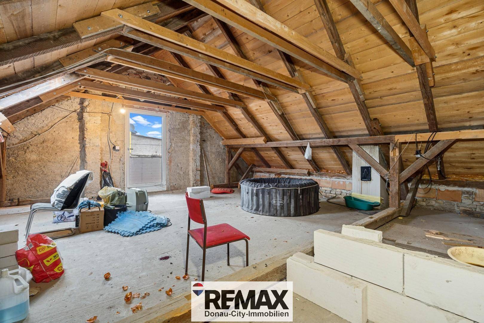 Unausgebauter Dachboden mit sichtbaren Holzbalken und einem Fenster, bereit zum Ausbau.
