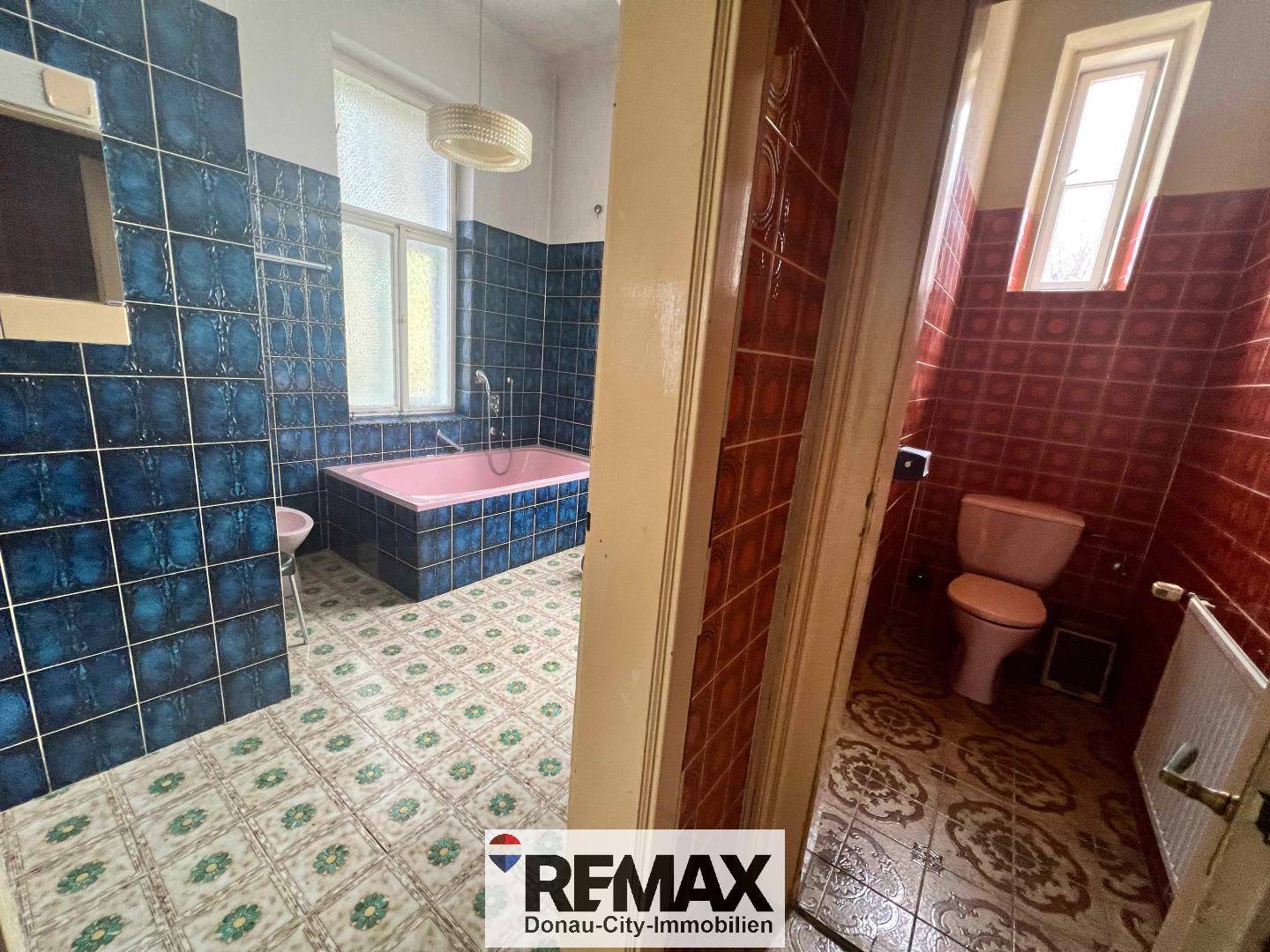 Badezimmer mit blauen Fliesen und rosa Badewanne, angrenzend an eine separate Toilette.