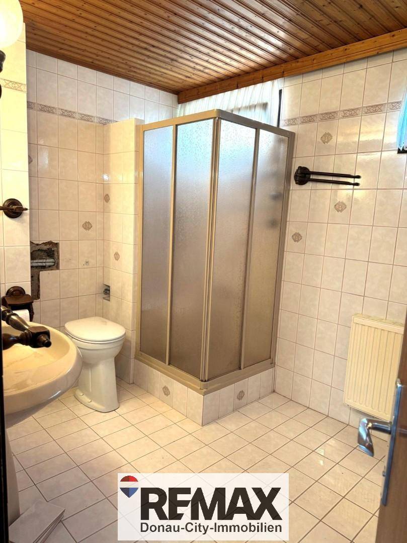 Badezimmer mit Fliesen, Duschkabine, WC und Waschbecken, ausgestattet mit Holzdecke.