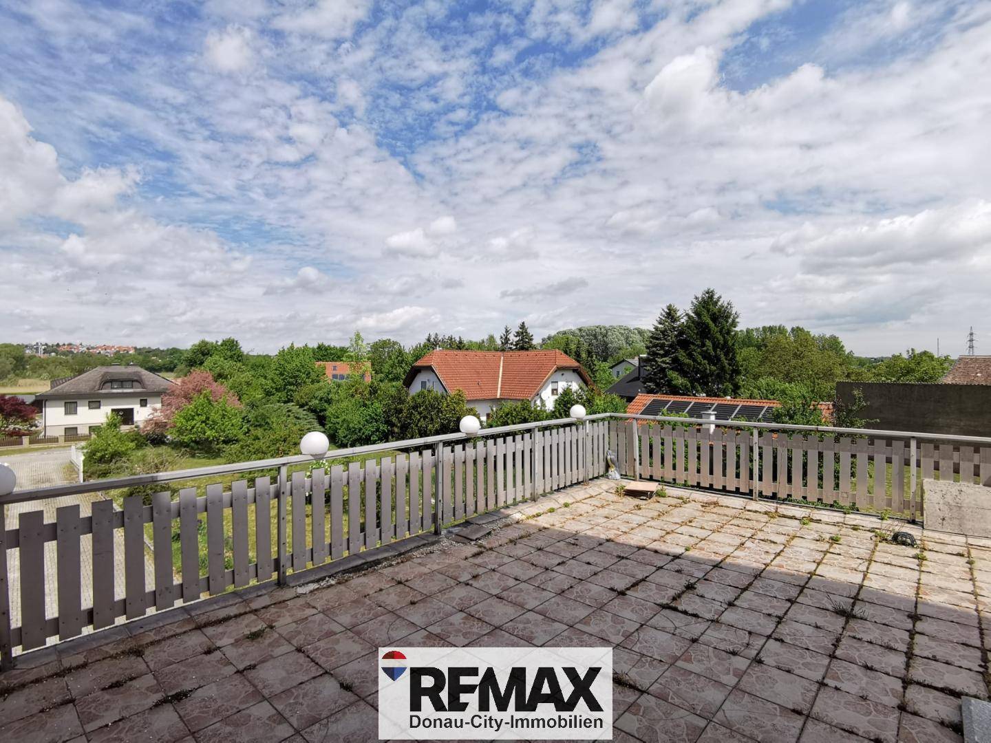 Große Außenterrasse mit Fliesenboden, Holzgeländer und weitem Blick über die Umgebung.