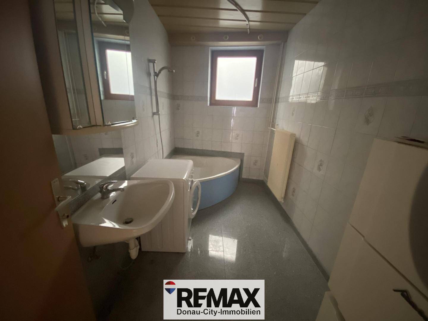 Badezimmer mit Badewanne, Waschbecken, Fenster und Fliesen an Wänden und Boden.
