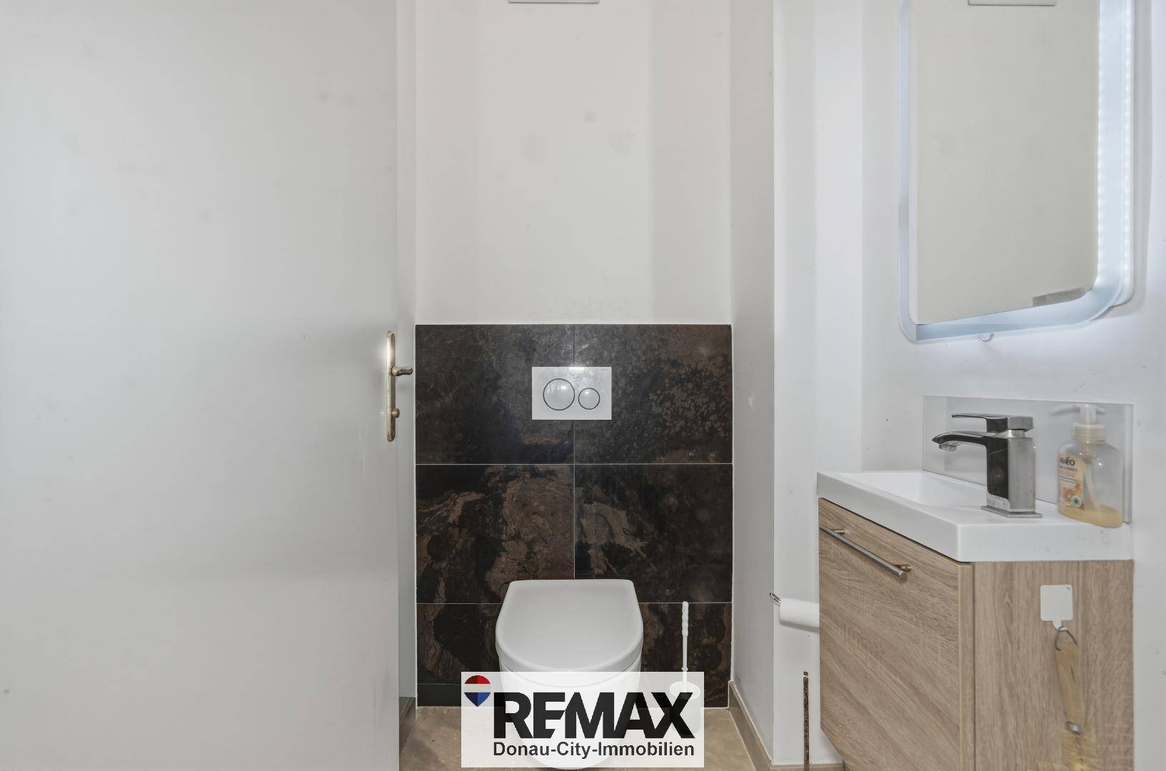 Modernes Gäste-WC mit Wand-WC, Waschbecken und dunklen Fliesen.