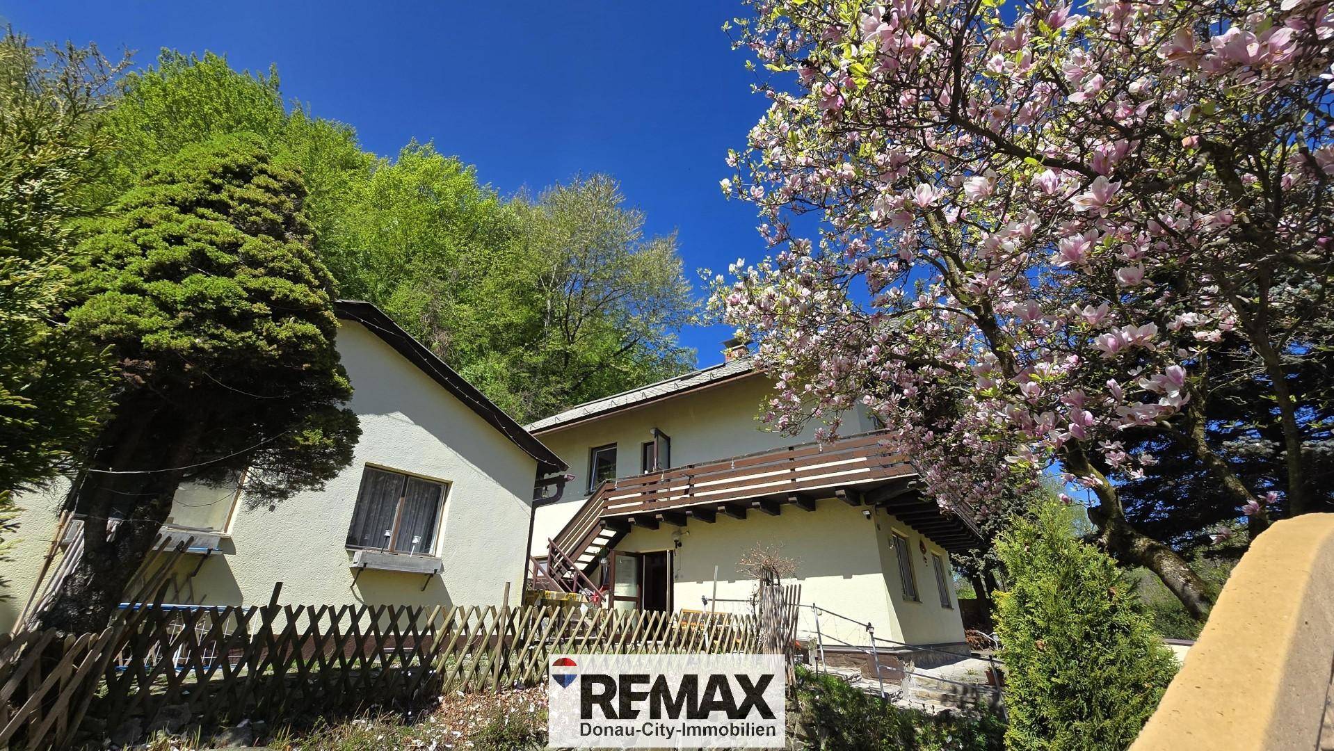Rückansicht des Hauses mit Balkon, Treppe und blühenden Bäumen.