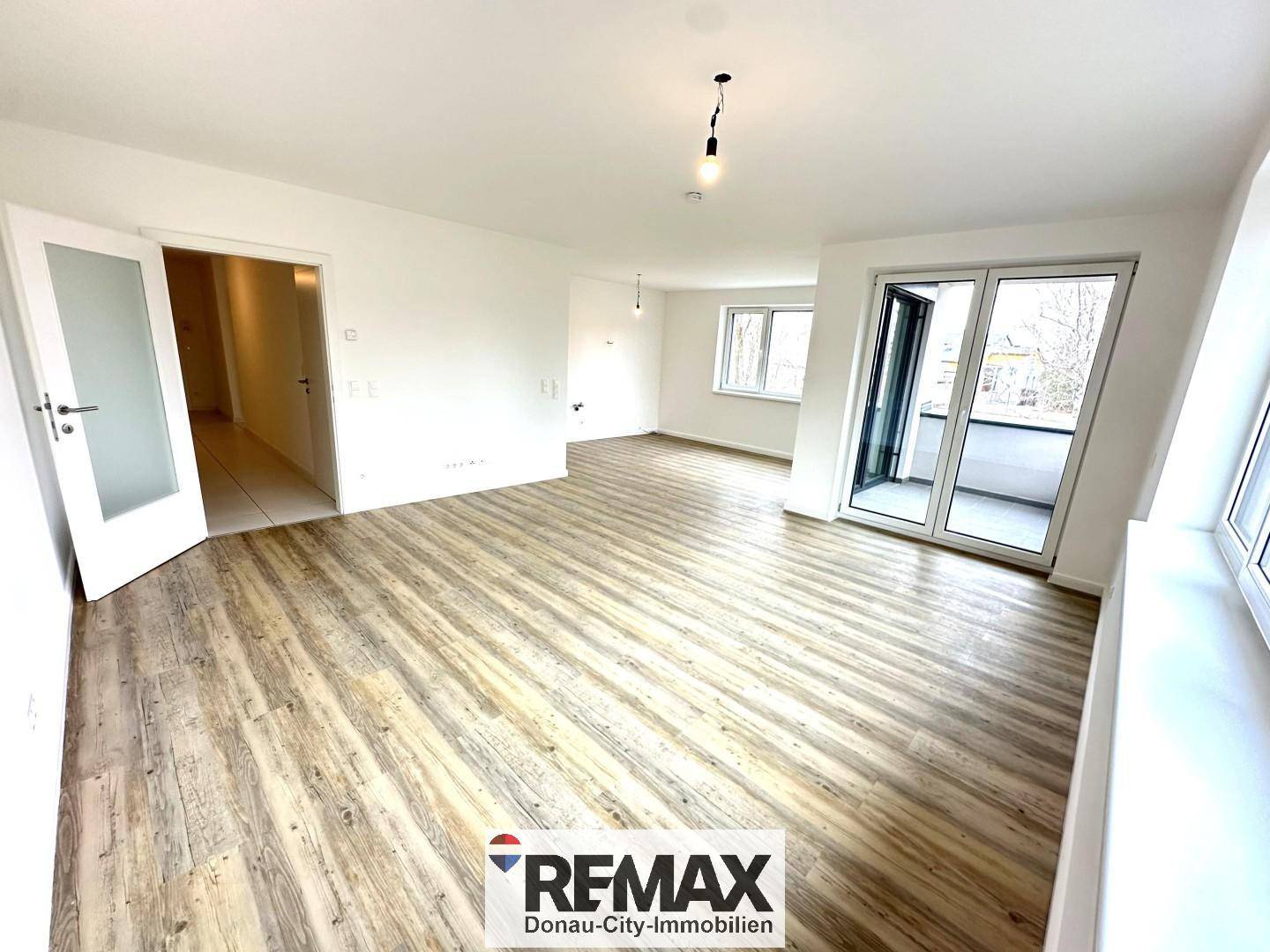 Helles, leeres Wohnzimmer mit modernem Laminatboden und Zugang zu einem Balkon.