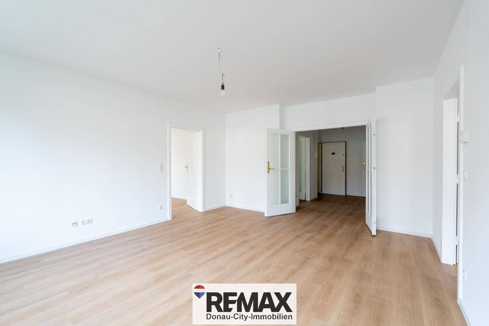 Geräumiger, heller Wohnbereich mit hellem Laminatboden und mehreren Türen.