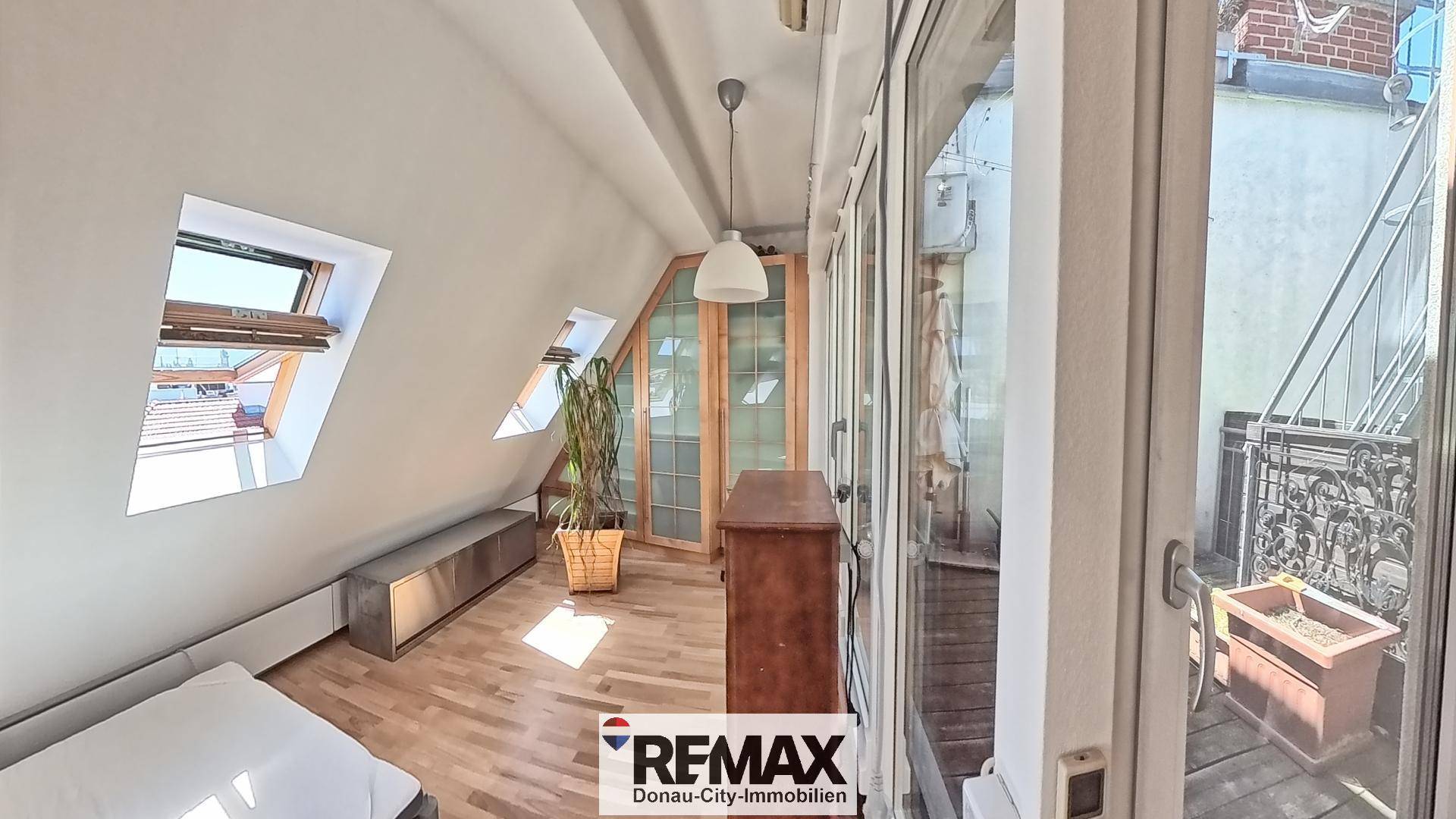 Dachgeschosszimmer mit Holzboden, Dachfenstern und Zugang zu einem kleinen Balkon.