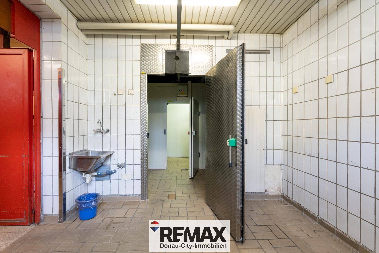 Gefliester Lagerraum mit großem Kühlraum und Waschbecken, ideal für gewerbliche Nutzung.