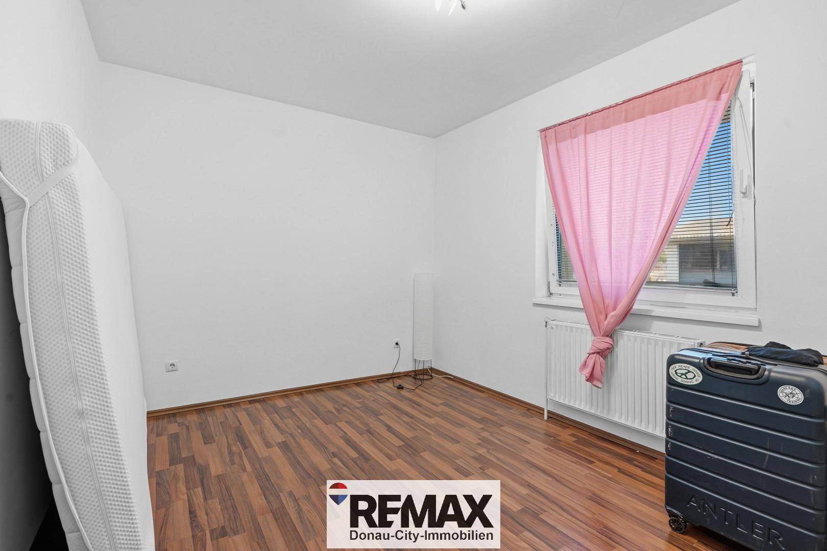 Leeres Schlafzimmer mit Laminatboden, Fenster und Heizkörper.