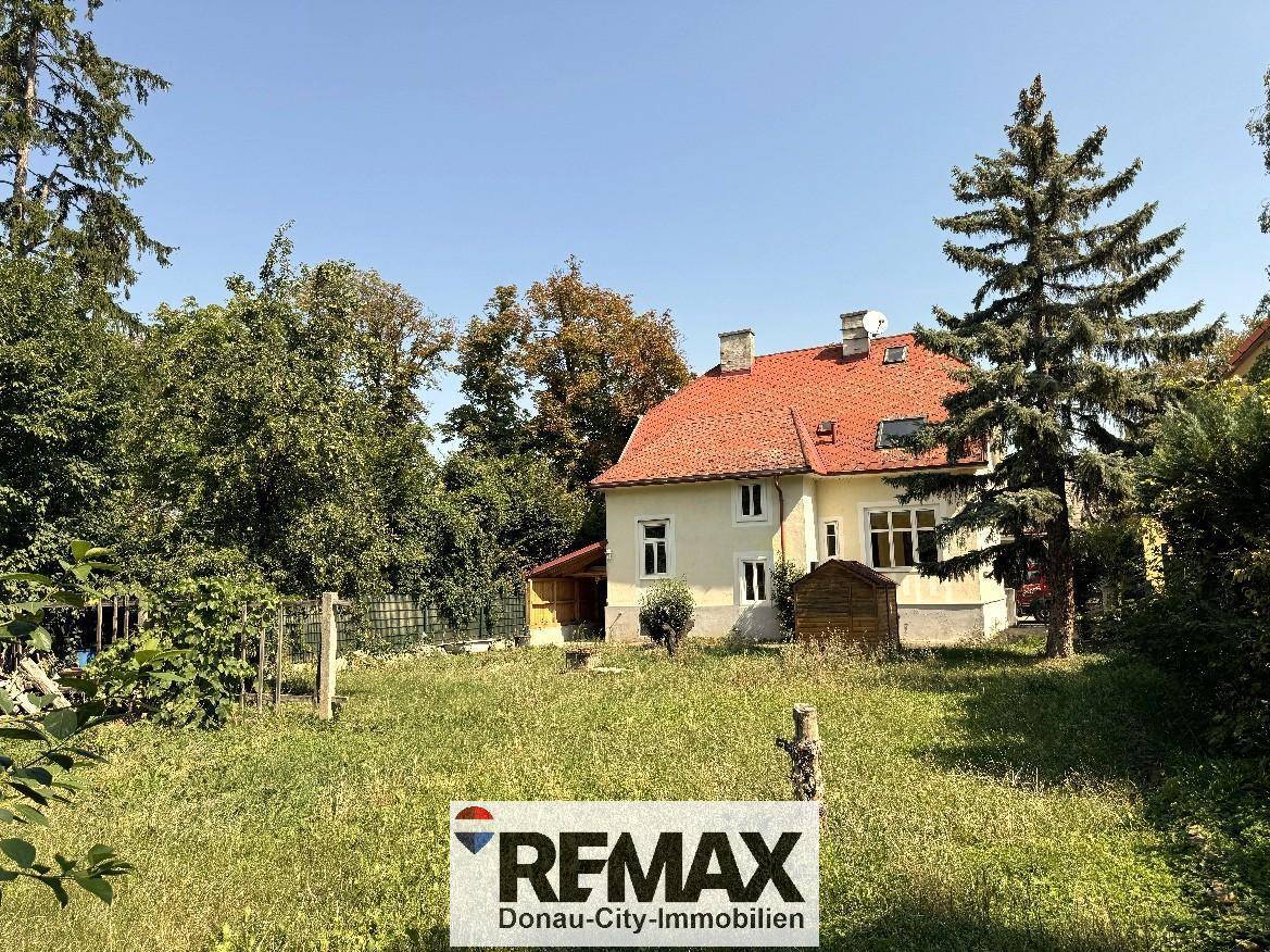 Das Haus von der Gartenseite, umgeben von einem weitläufigen Rasen und Bäumen.