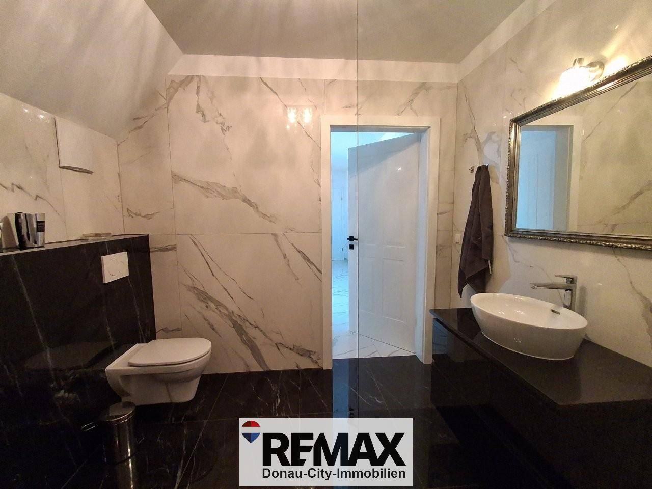 Modernes Badezimmer mit Marmorfliesen, Einzelwaschbecken und wandmontierter Toilette.