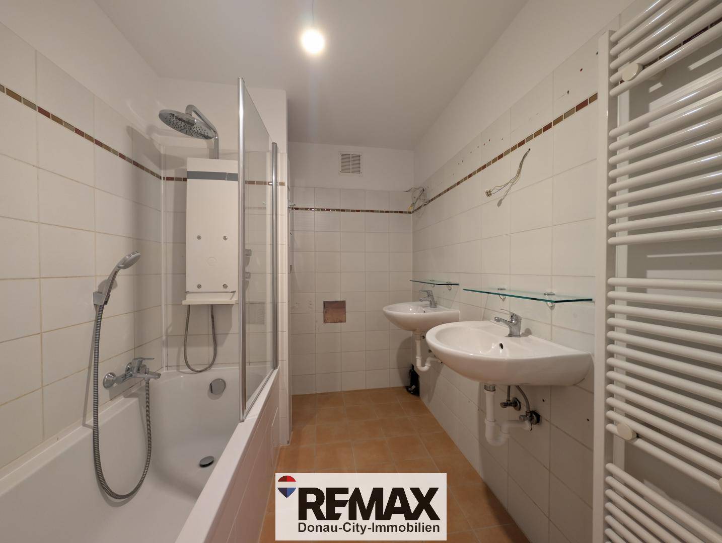 Gefliestes Badezimmer mit Badewanne, Duschabtrennung, zwei Waschbecken und Handtuchheizkörper.