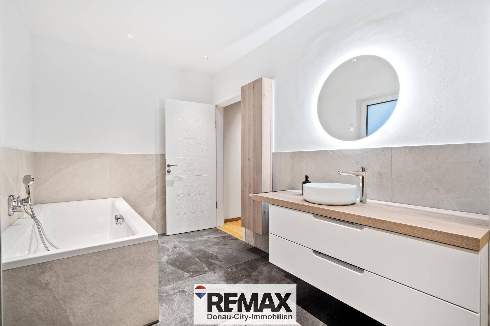 Helles Badezimmer mit Badewanne, modernem Waschtisch und beleuchtetem Spiegel.