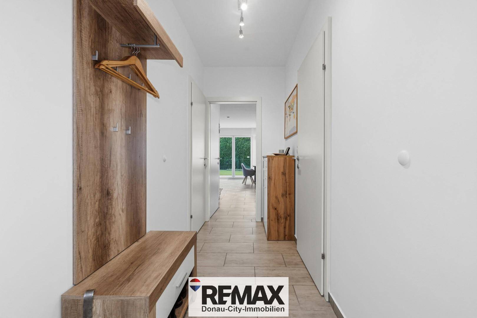 Heller Flur mit Garderobe aus Holz und Fliesenboden, der zu den weiteren Räumen führt.