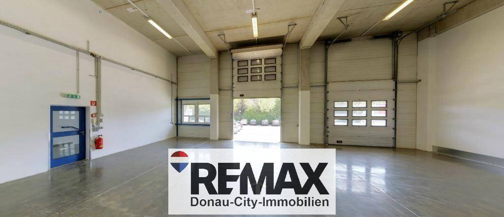 Geräumige Lagerhalle mit Betonboden, hohen Decken und großen Rolltoren für den Zugang und die Belieferung.