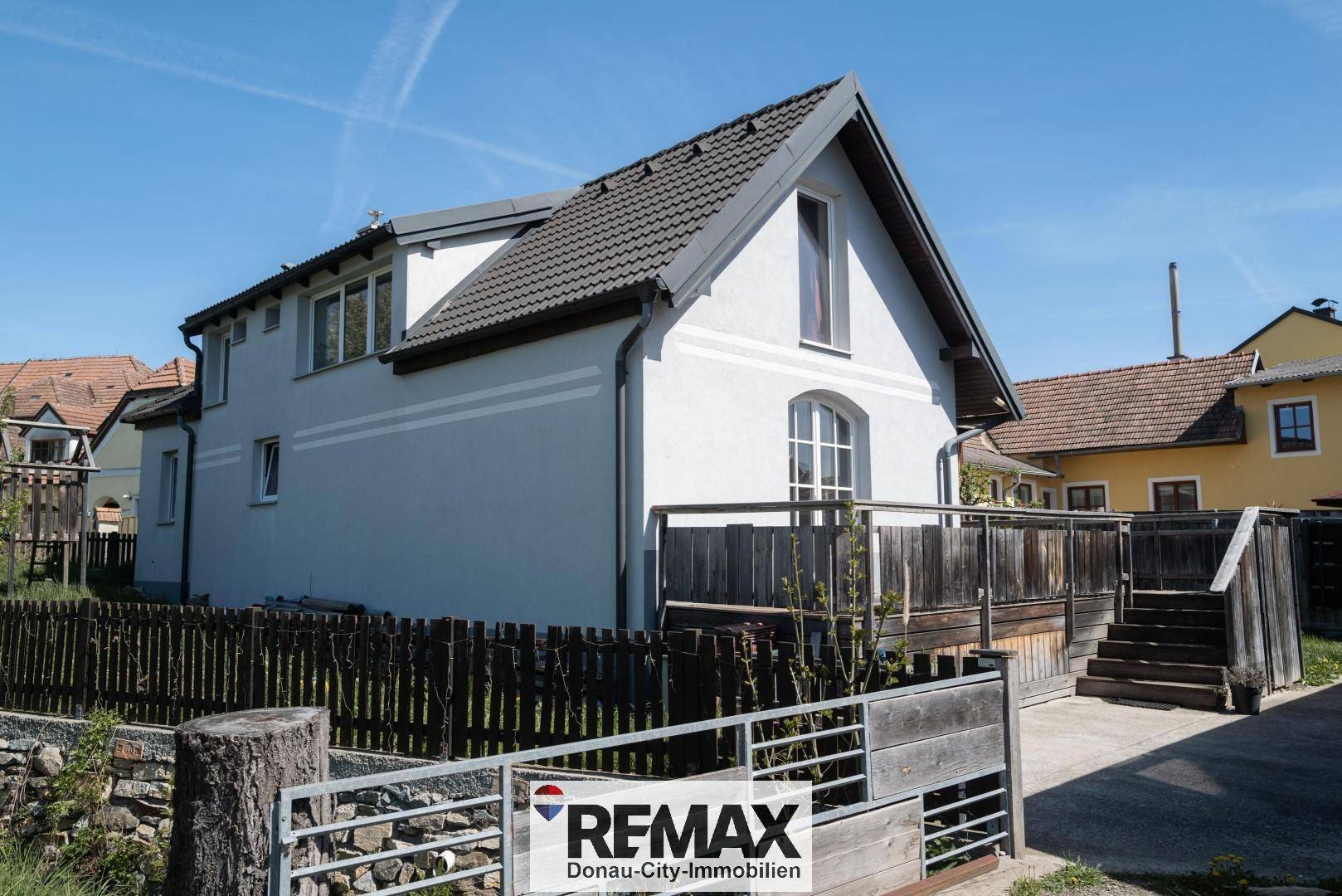 Modernes Einfamilienhaus mit heller Fassade, dunklem Dach und einem kleinen Gartenbereich.