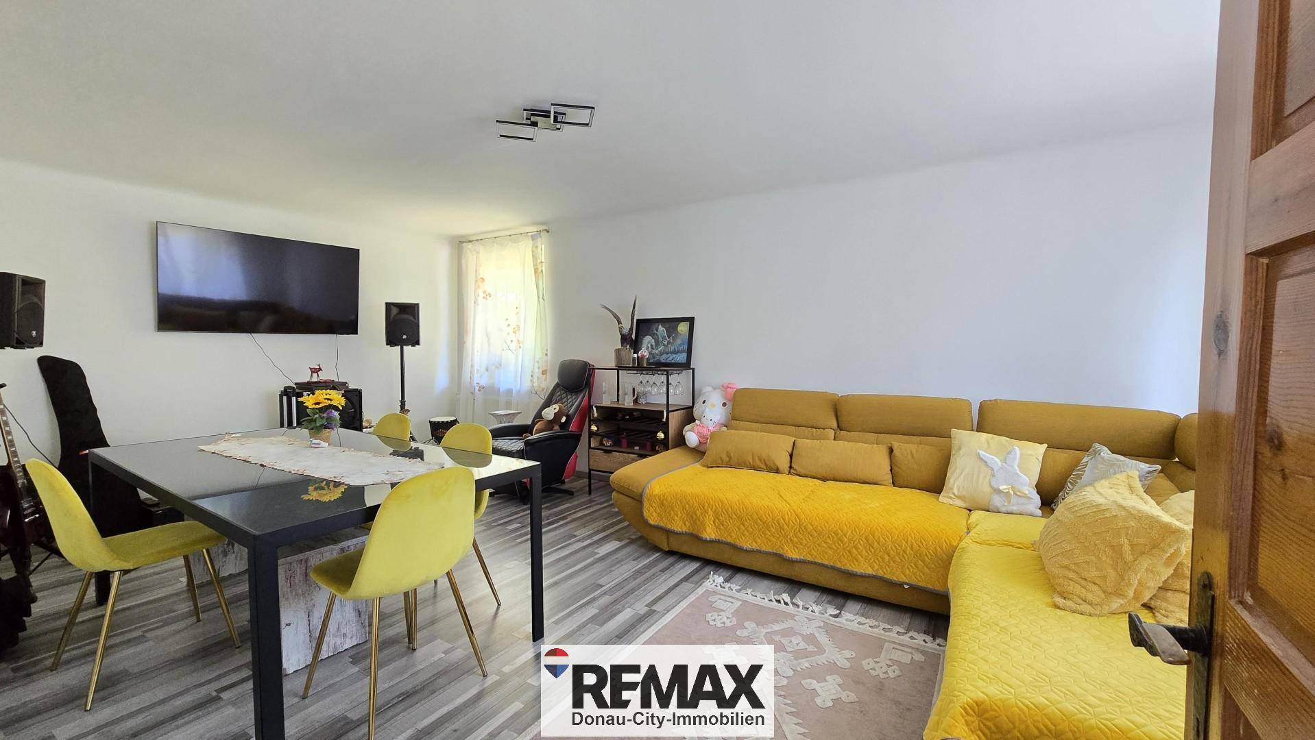 Geräumiger Wohn-Essbereich mit gelbem Sofa, Esstisch und Fernseher.