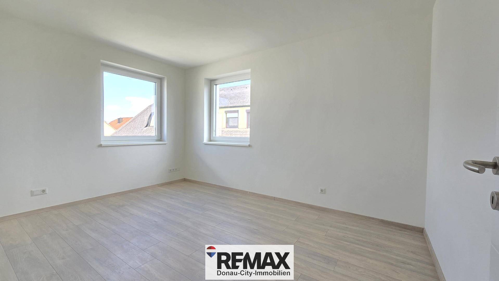 Leeres Schlafzimmer mit hellem Laminatboden und zwei Fenstern für viel Tageslicht.