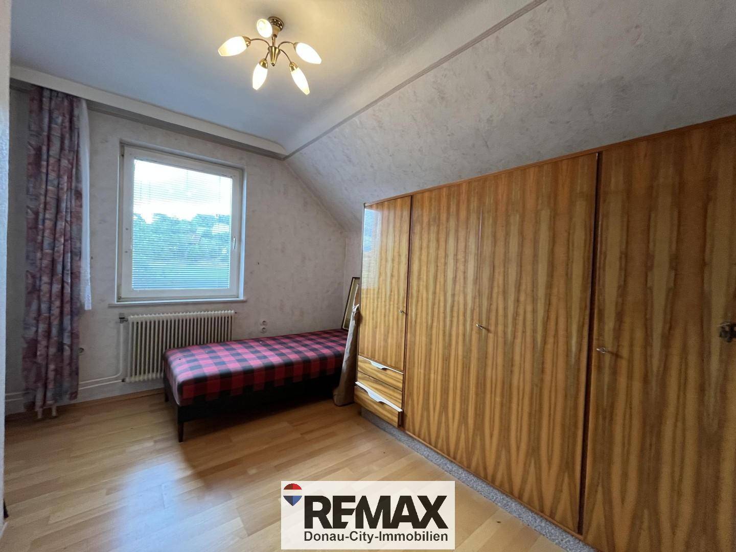 Schlafzimmer mit Einzelbett, großem Holzschrank und Fenster, mit Dachschräge.