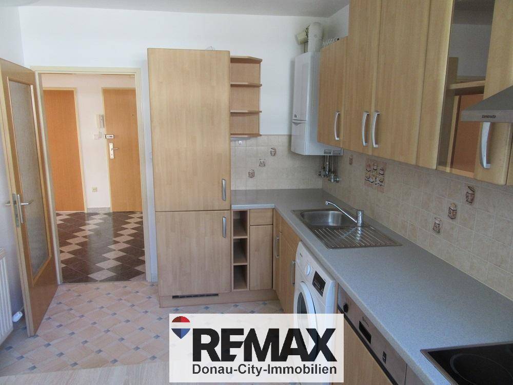 Funktionale Küche mit Holzschränken, Spüle und Waschmaschine, Blick in den Flur.