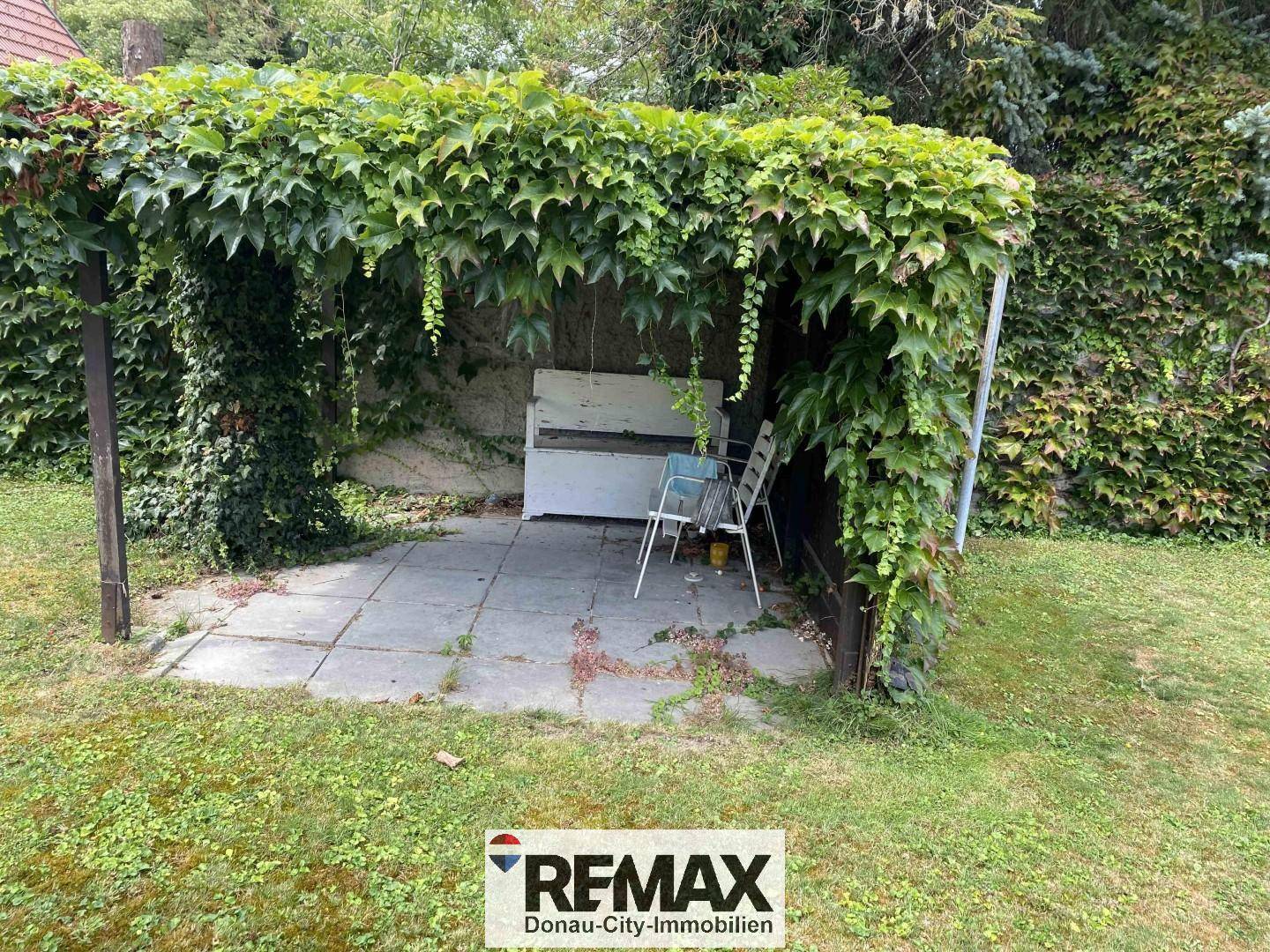 Überdachter Sitzbereich im Garten, umgeben von üppigem Grün.