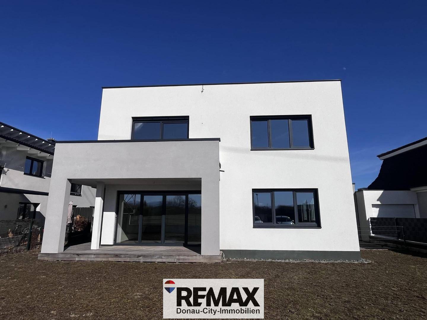 Rückseite des modernen Hauses mit großer Rasenfläche und Terrasse.