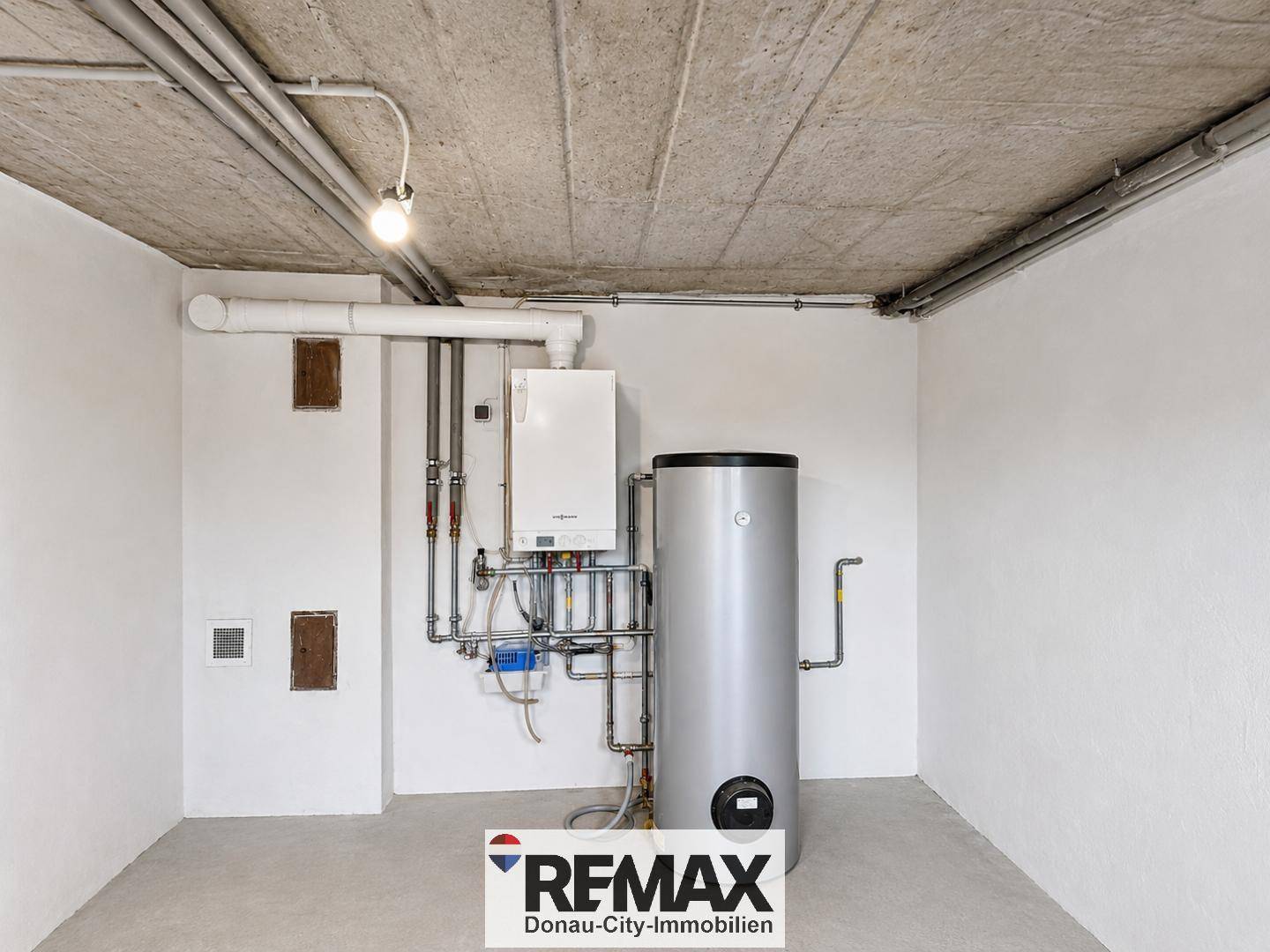 Detailansicht der Heizungsanlage und des Warmwasserspeichers in einem sauberen Kellerraum.