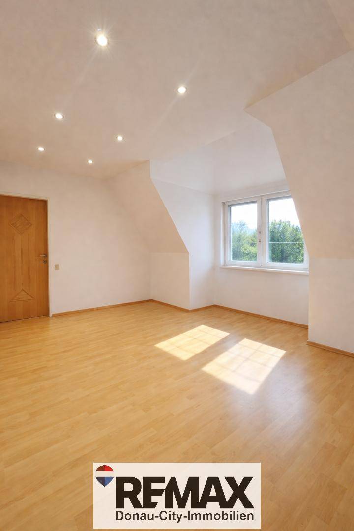Heller, leerer Raum mit Dachschrägen, einem Fenster und hellem Holzfußboden, ideal als Schlafzimmer.