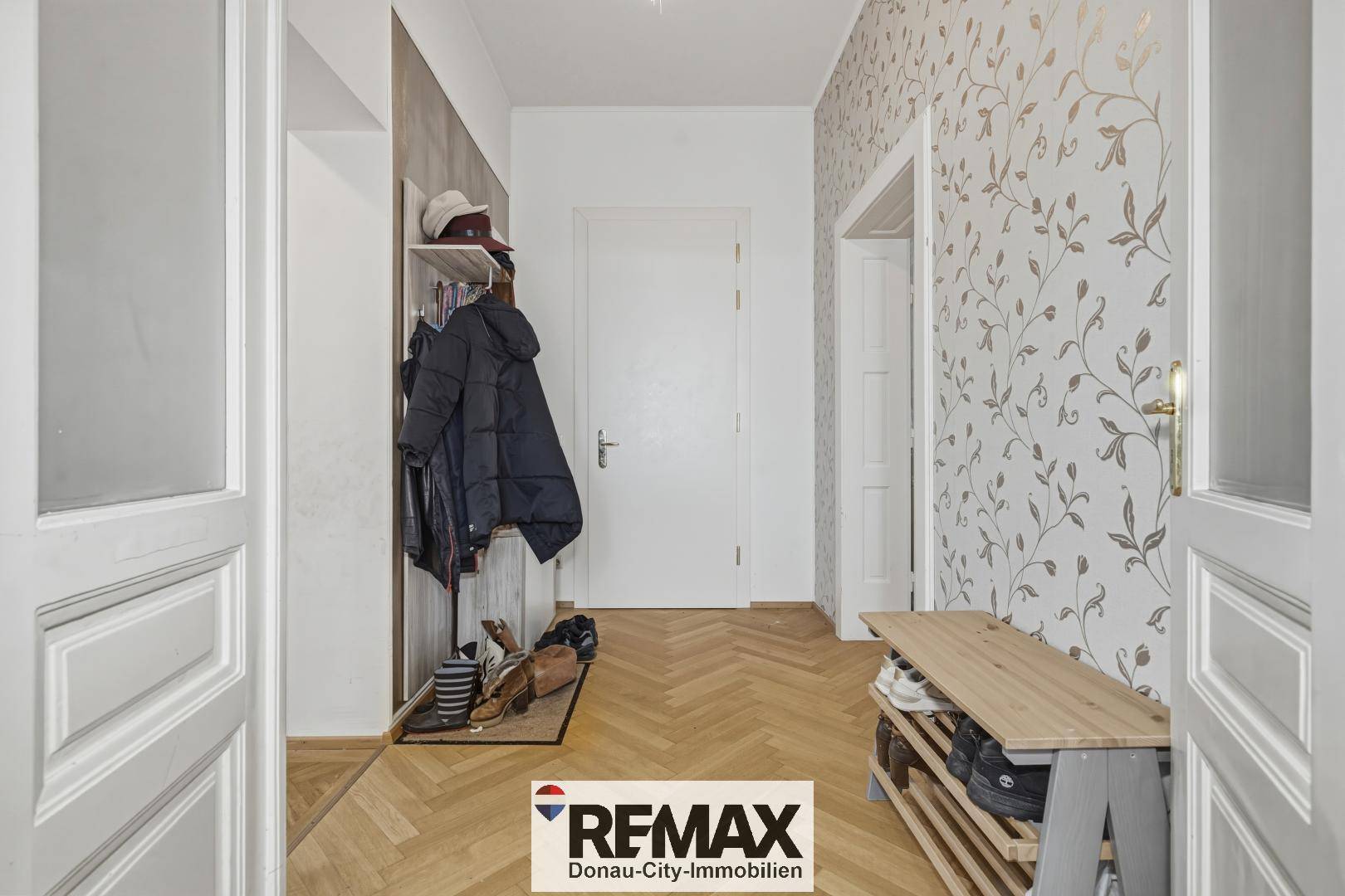 Eingangsbereich mit Fischgrätparkett, Garderobe und dekorativer Tapete.