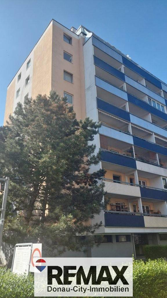 Mehrstöckiges Wohngebäude mit blauen und beigen Balkonen unter klarem Himmel.