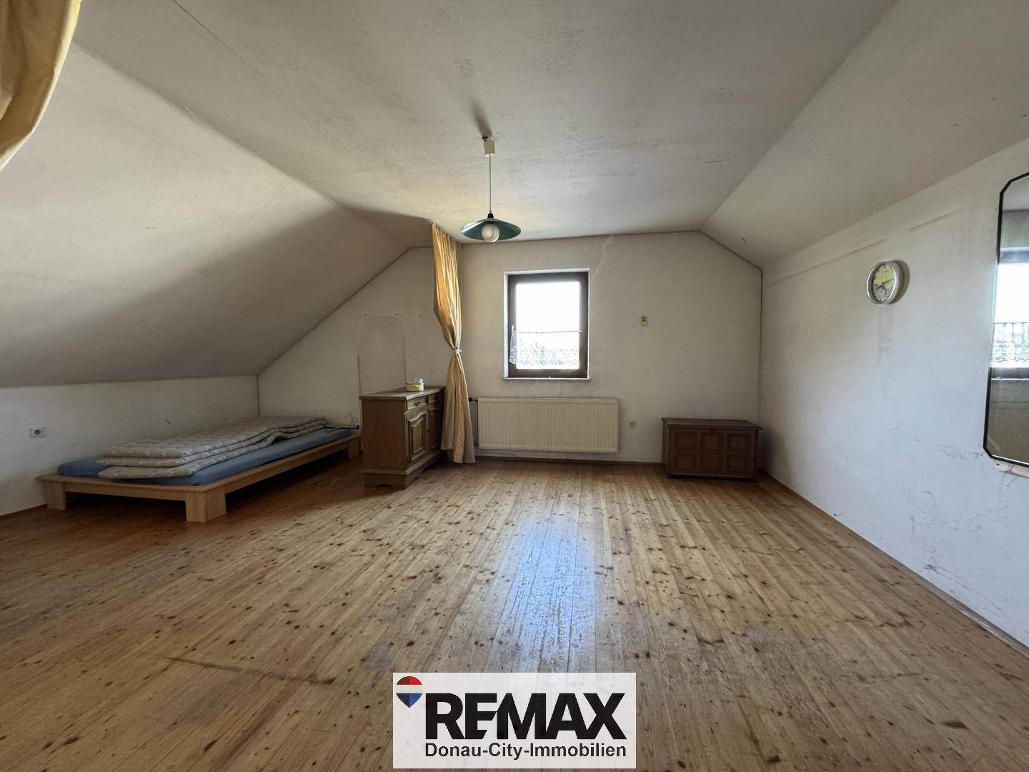 Dachgeschoss-Schlafzimmer mit schrägen Wänden, Holzdielenboden, einem Bett und einem Fenster für natürliches Licht.