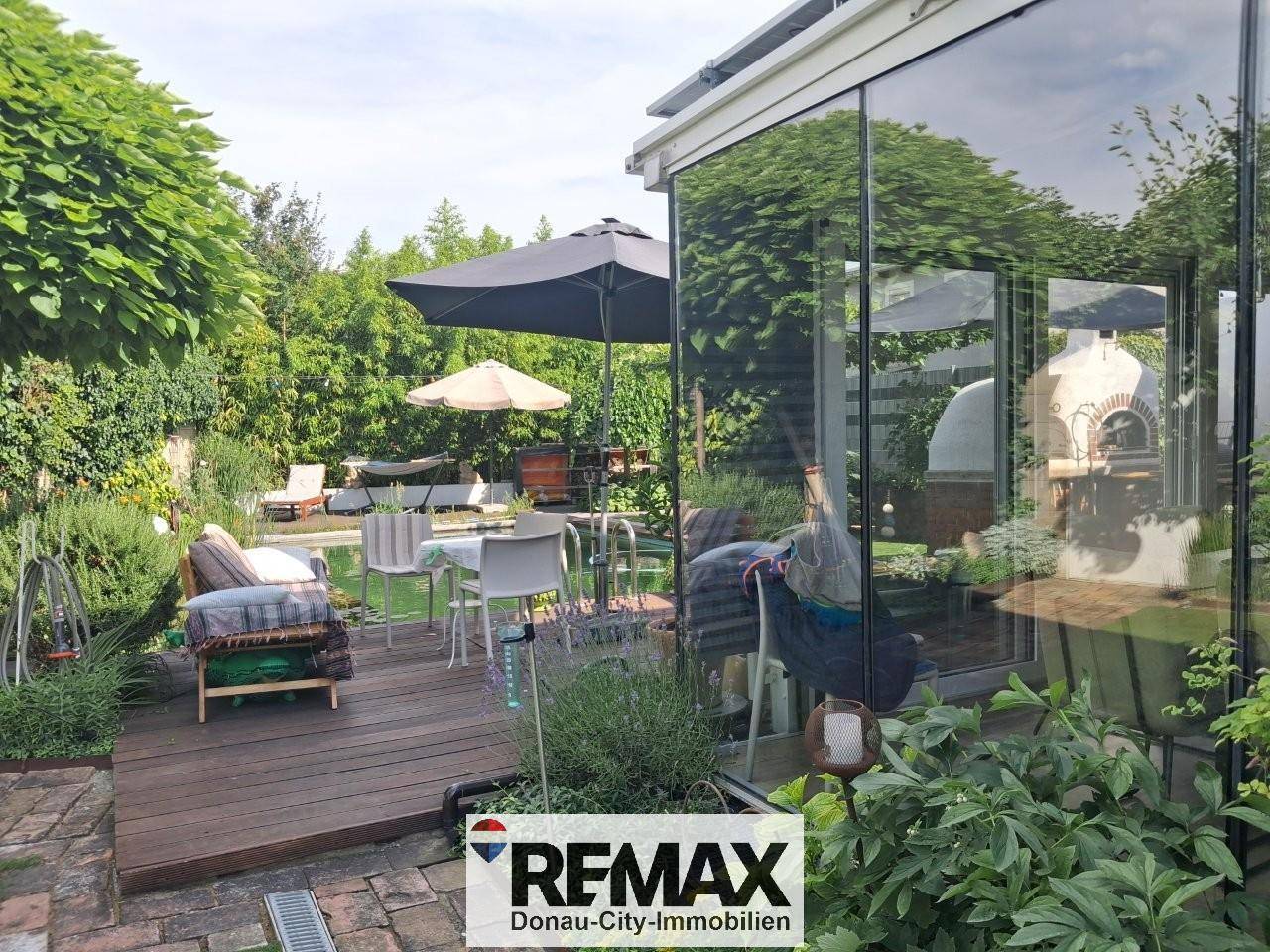 Sonniger Terrassenbereich mit Sitzgelegenheiten, Pizzaofen und Zugang zum Wintergarten.