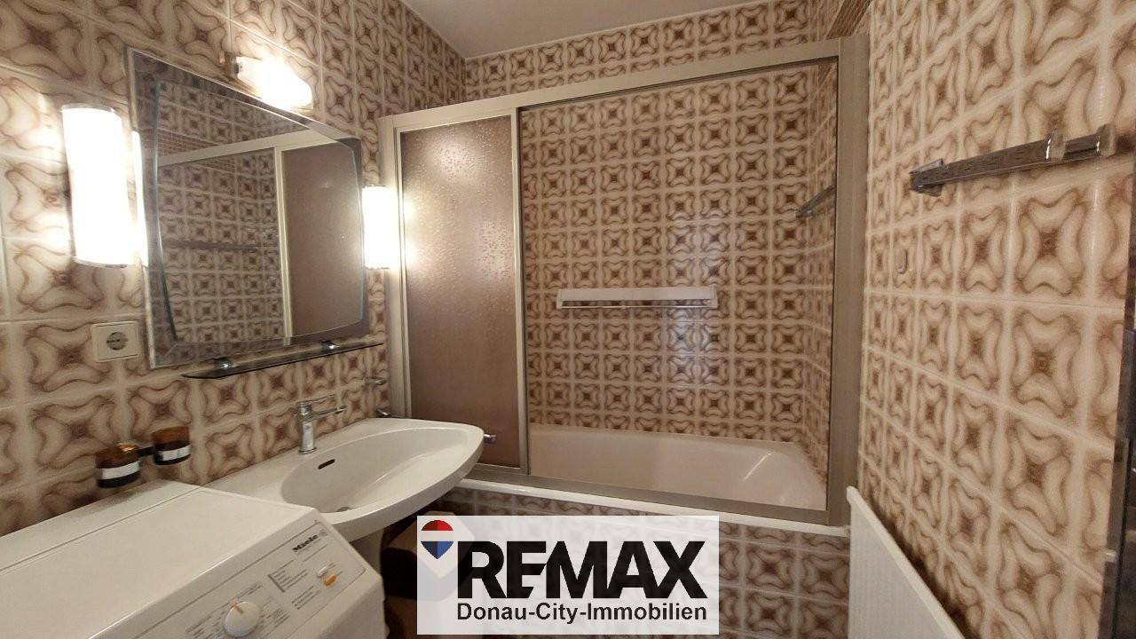 Badezimmer mit gemusterten Fliesen, Badewanne mit Duschabtrennung und Waschbecken.