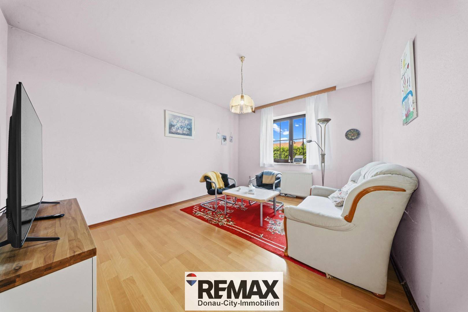 Helles Zimmer mit Laminatboden, Sitzgelegenheiten und Fernseher, vielseitig nutzbar.