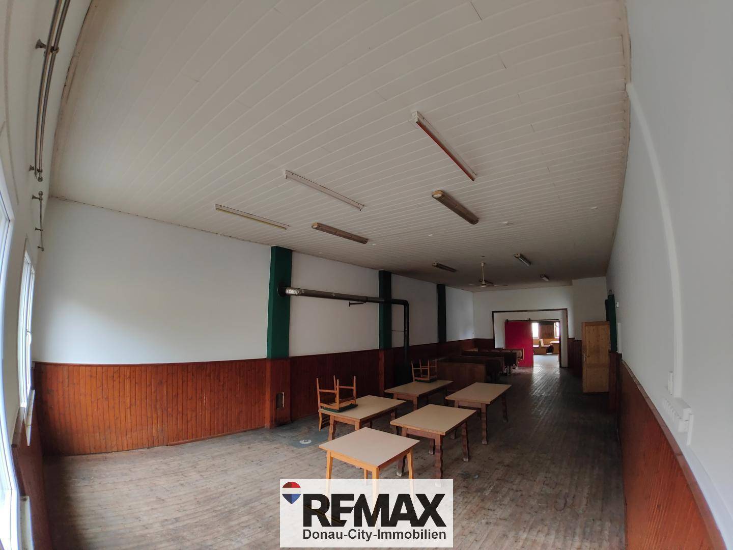 Geräumiger Saal mit Holzboden, Holztischen und Bänken, bereit für Veranstaltungen.
