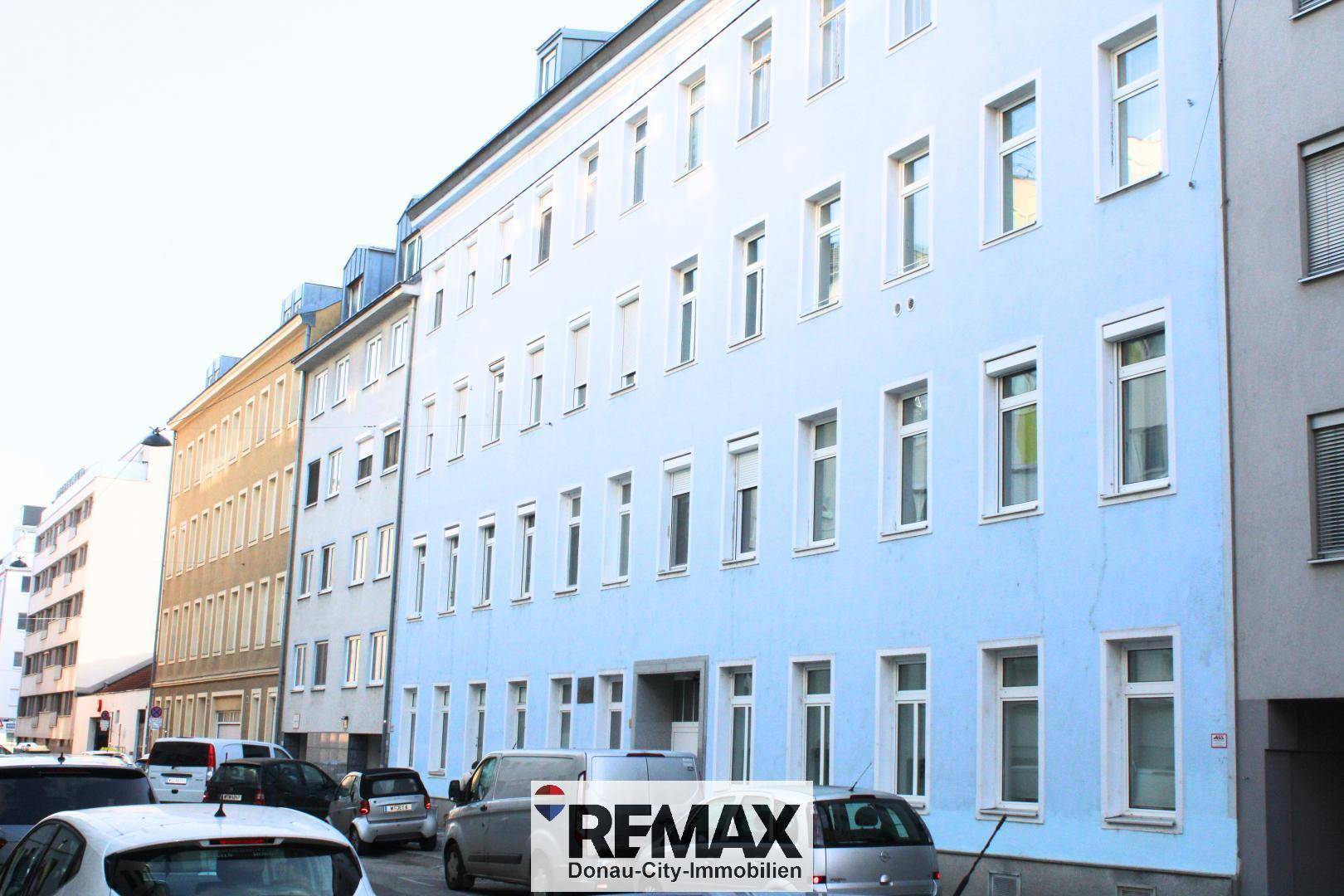 Mehrstöckiges Wohngebäude mit hellblauer Fassade und vielen Fenstern an einer Straße.