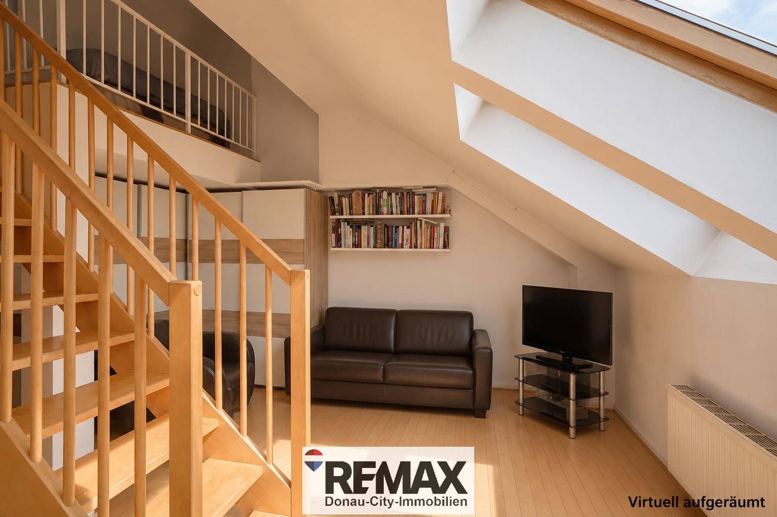 Gemütliches Wohnzimmer mit Sofa, Fernseher und Bücherregal unter einer Dachschräge mit Oberlicht.