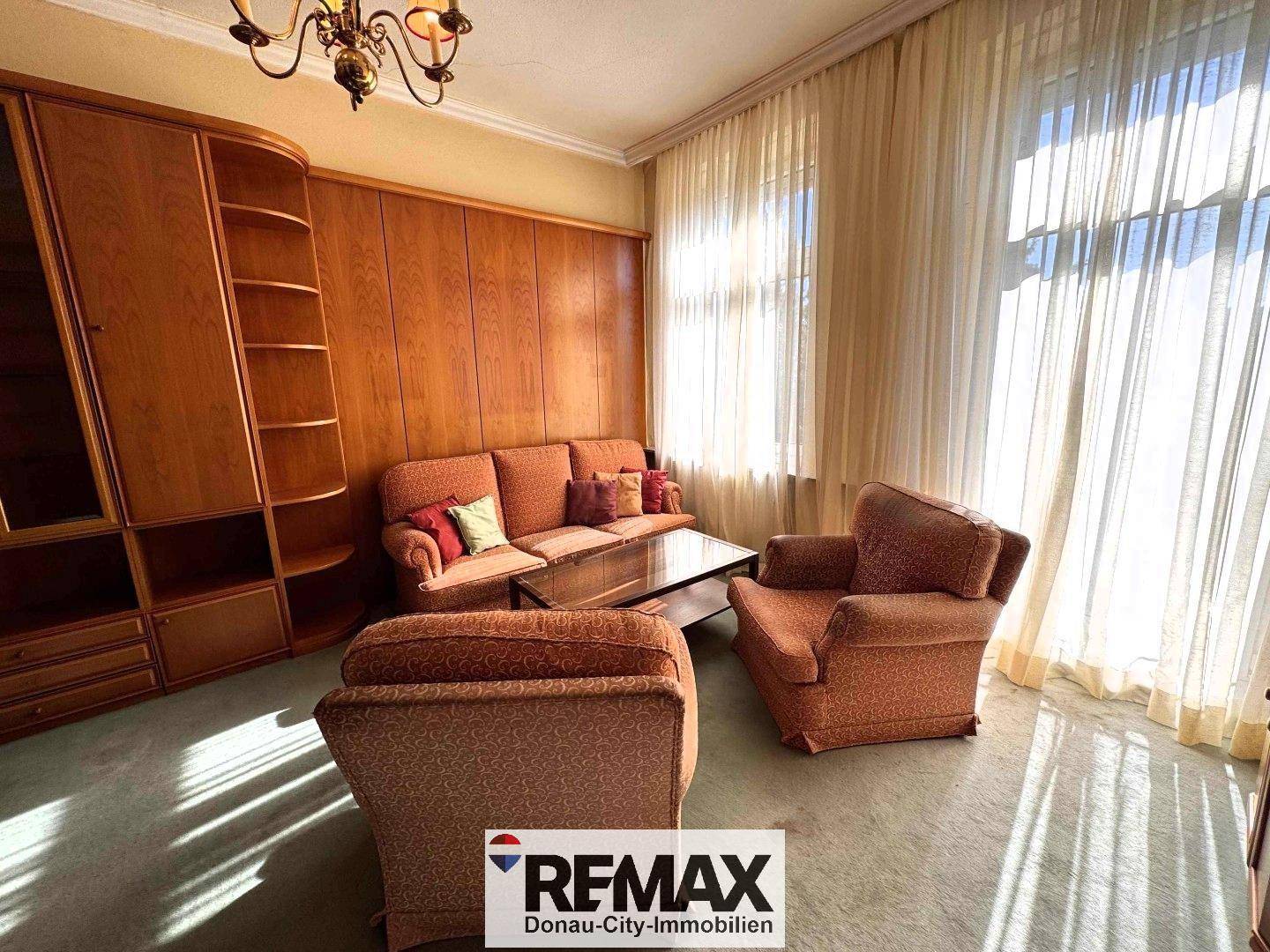 Helles Wohnzimmer mit großem Fenster, Teppichboden und umfangreicher Holzschrankwand, klassisch eingerichtet.