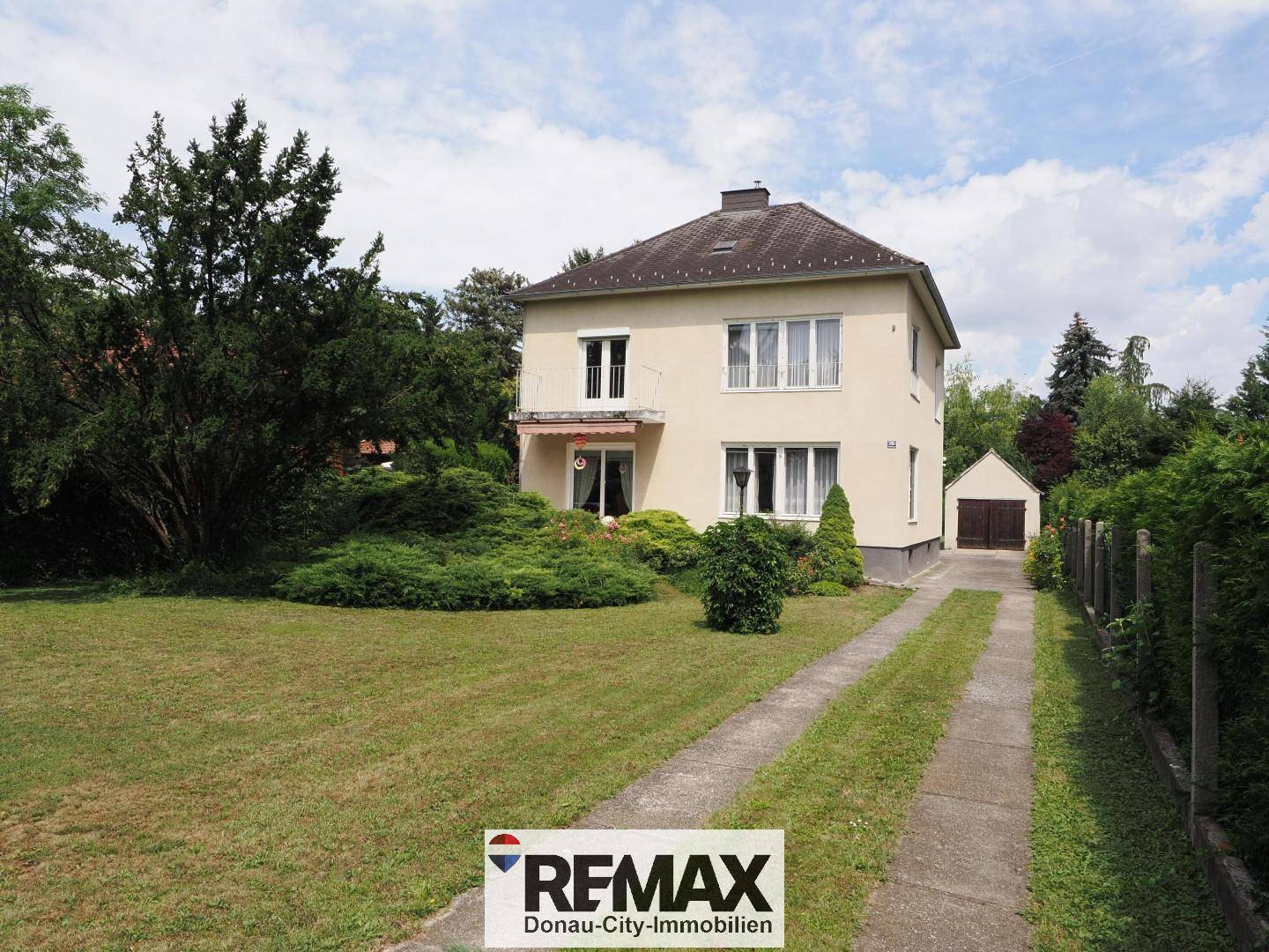 Freistehendes Haus mit heller Fassade, großem Garten und separater Garage.
